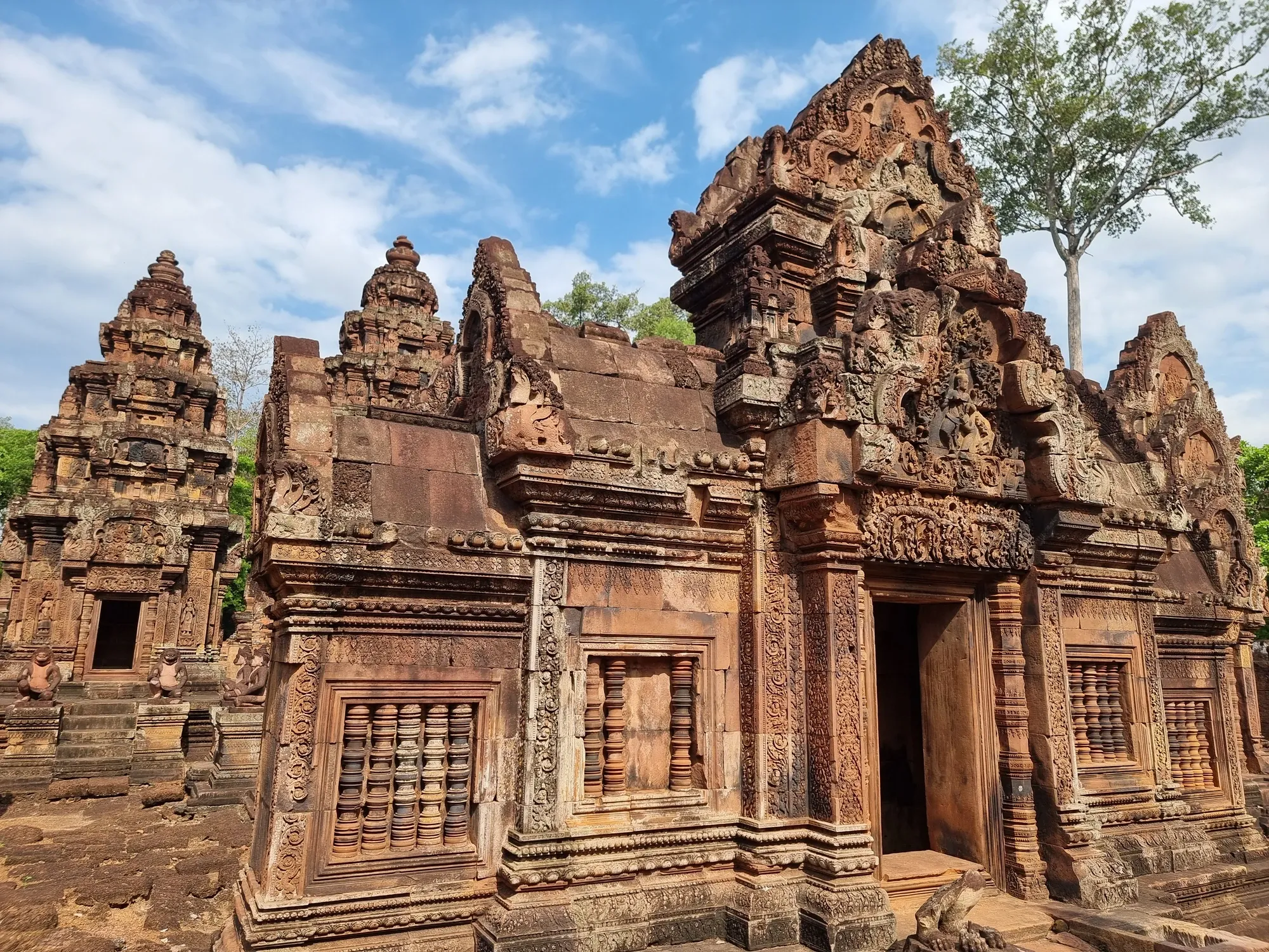 Un sanctuaire de Banteay Srei en grès rose, aux fenêtres à balustres et aux frontons finement sculptés, sous un ciel bleu