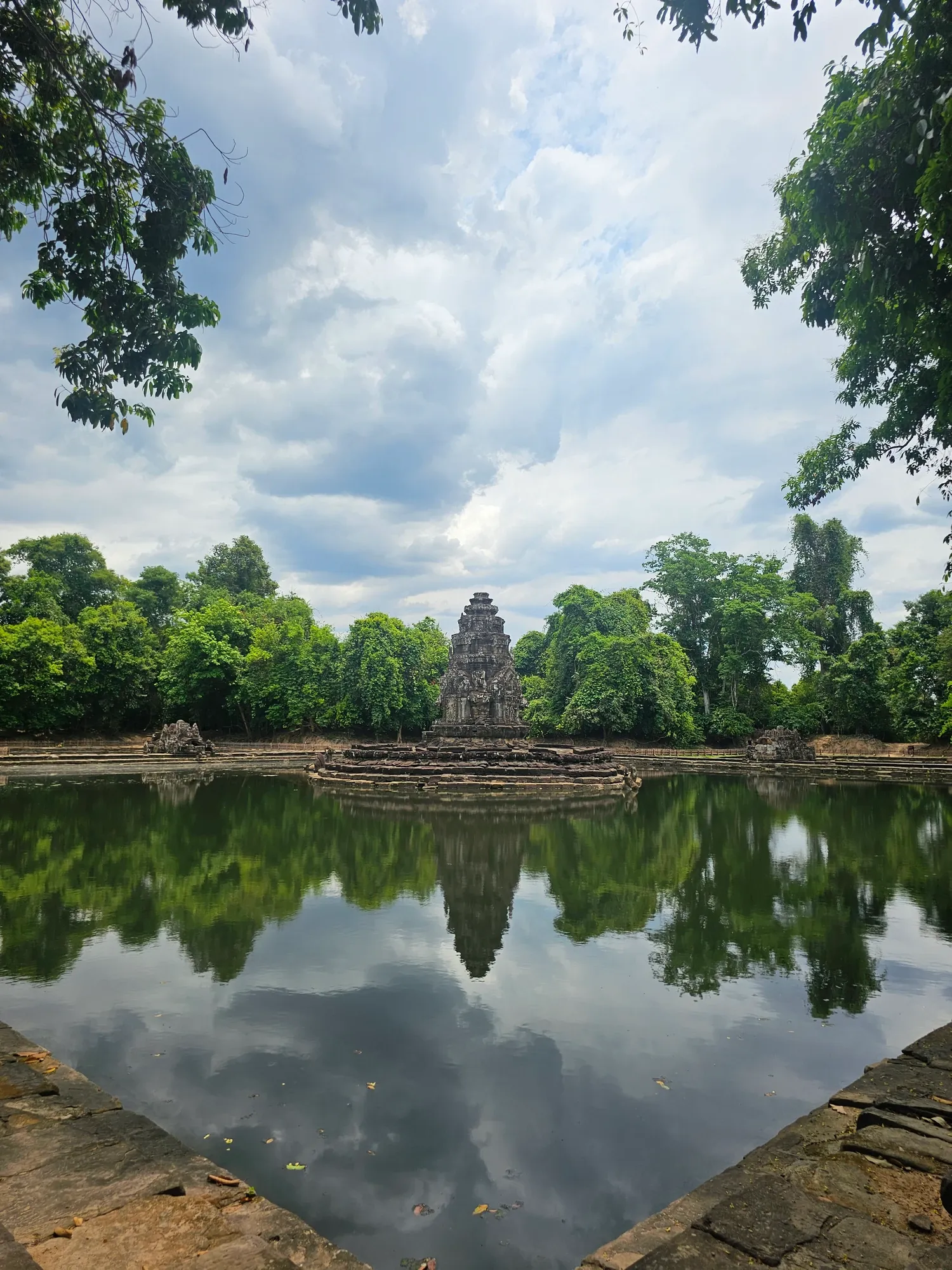 La petite tour de Neak Pean au centre de son bassin, qui se reflète dans l'eau sous les nuages