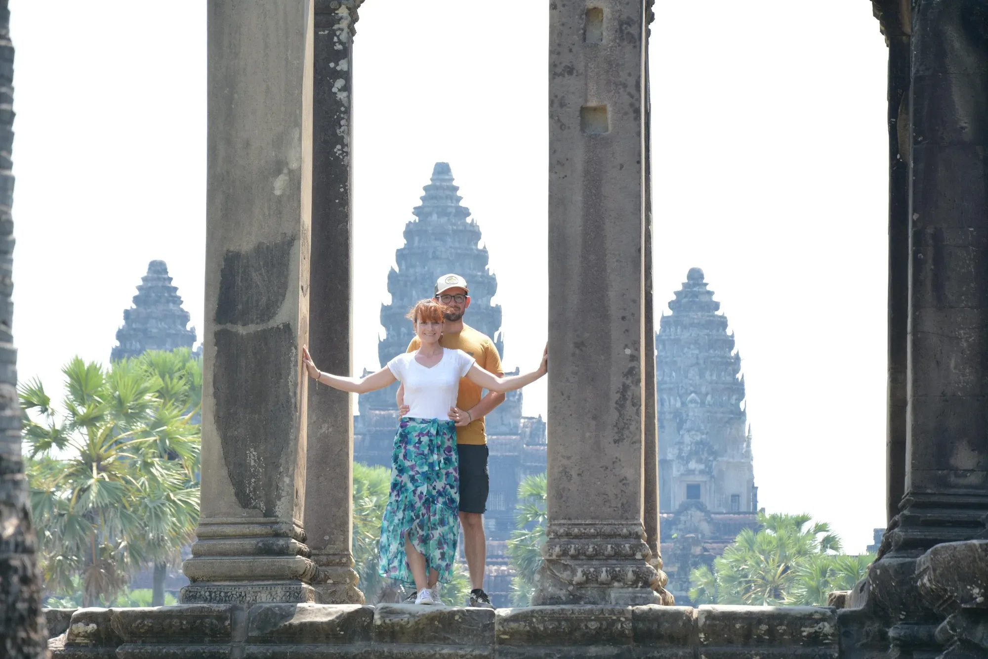Ségolène, bras écartés, et Antoine, juste derrière elle, entre deux colonnes de pierre, face aux tours d'Angkor Wat