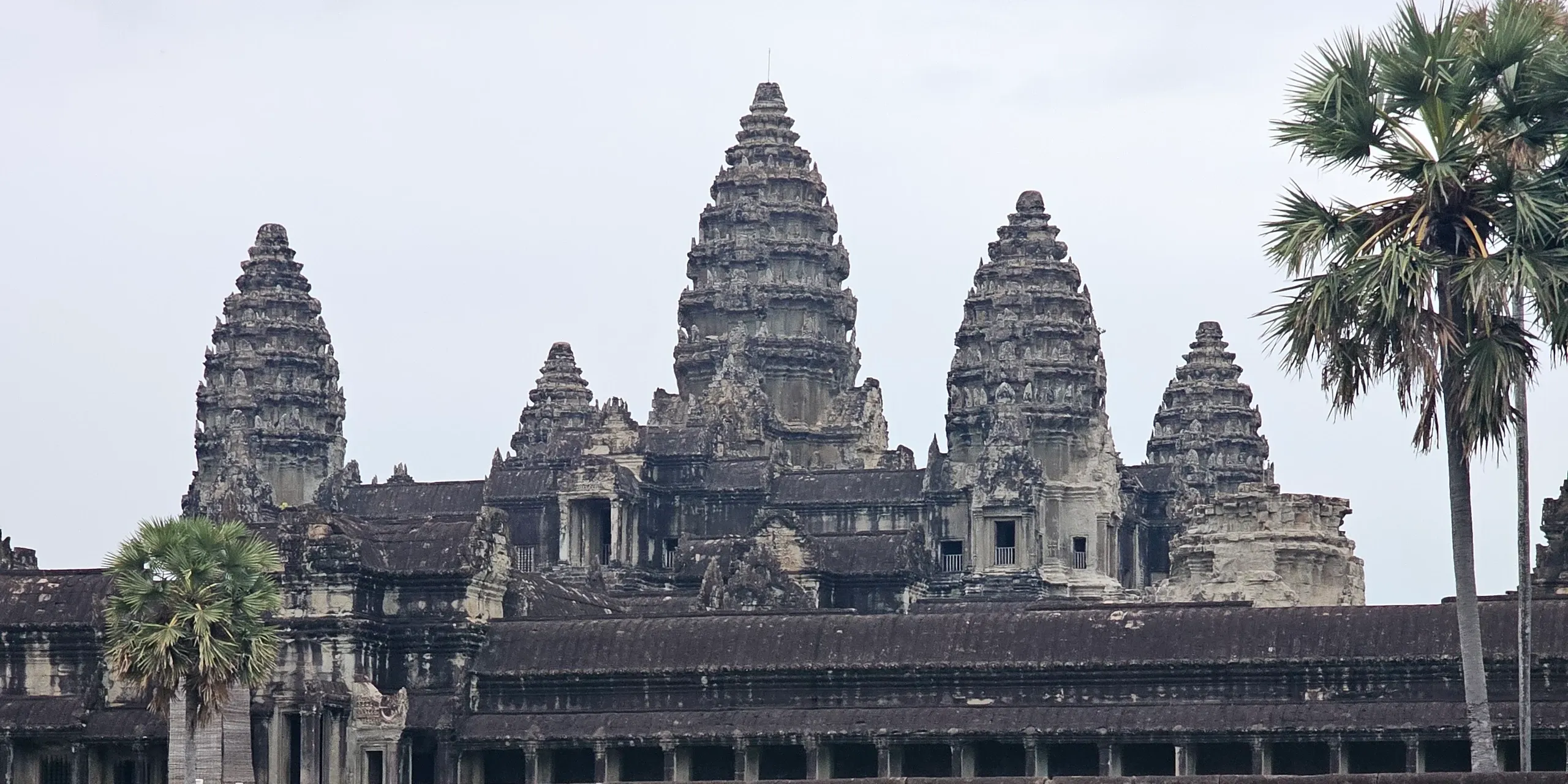 Les tours d'Angkor Wat sous le ciel gris du petit matin, au-dessus de la longue galerie du temple, avec des palmiers au premier plan, près de Siem Reap, au Cambodge