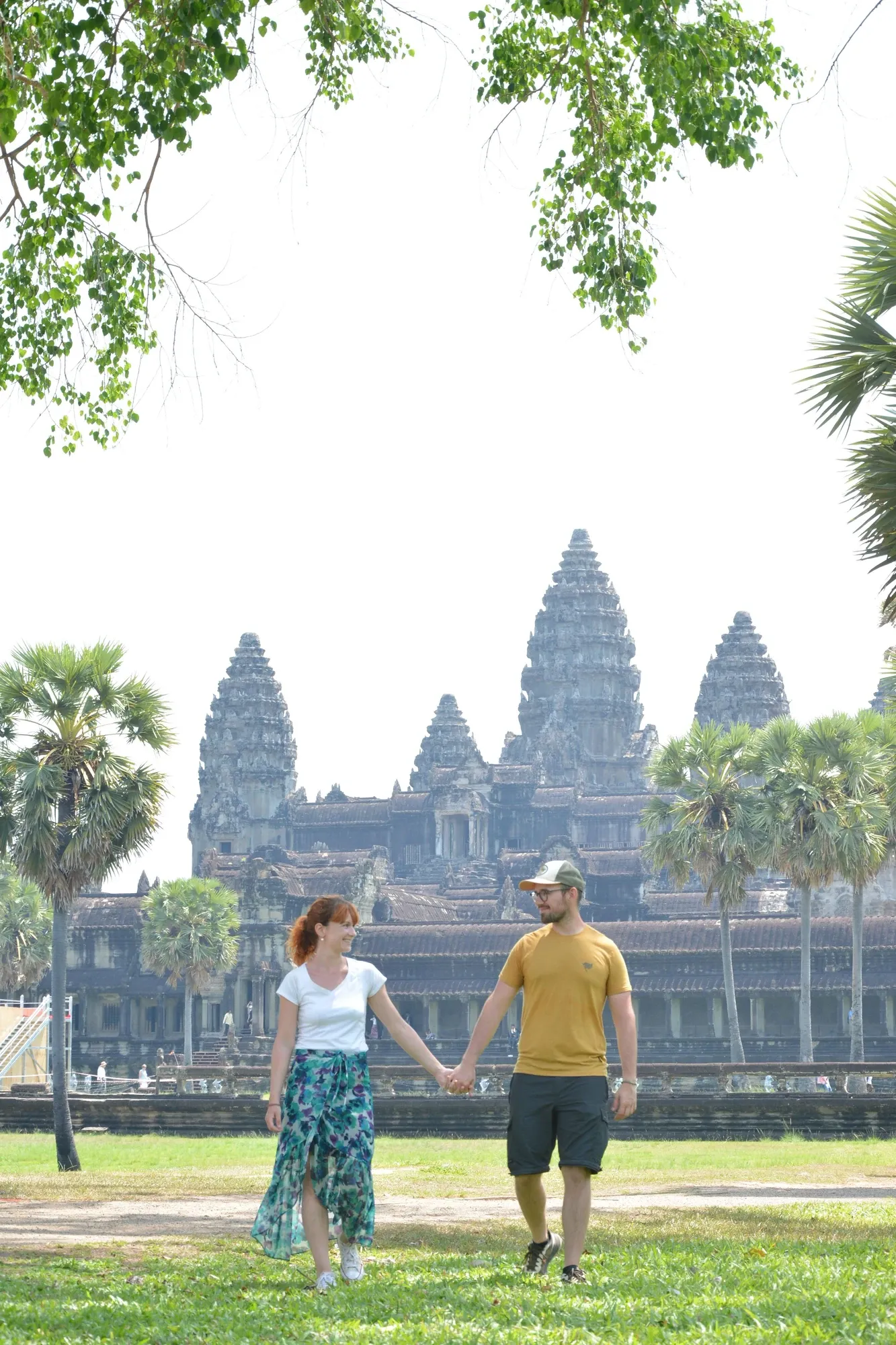 Ségolène et Antoine marchent main dans la main sur la pelouse, devant Angkor Wat et ses palmiers