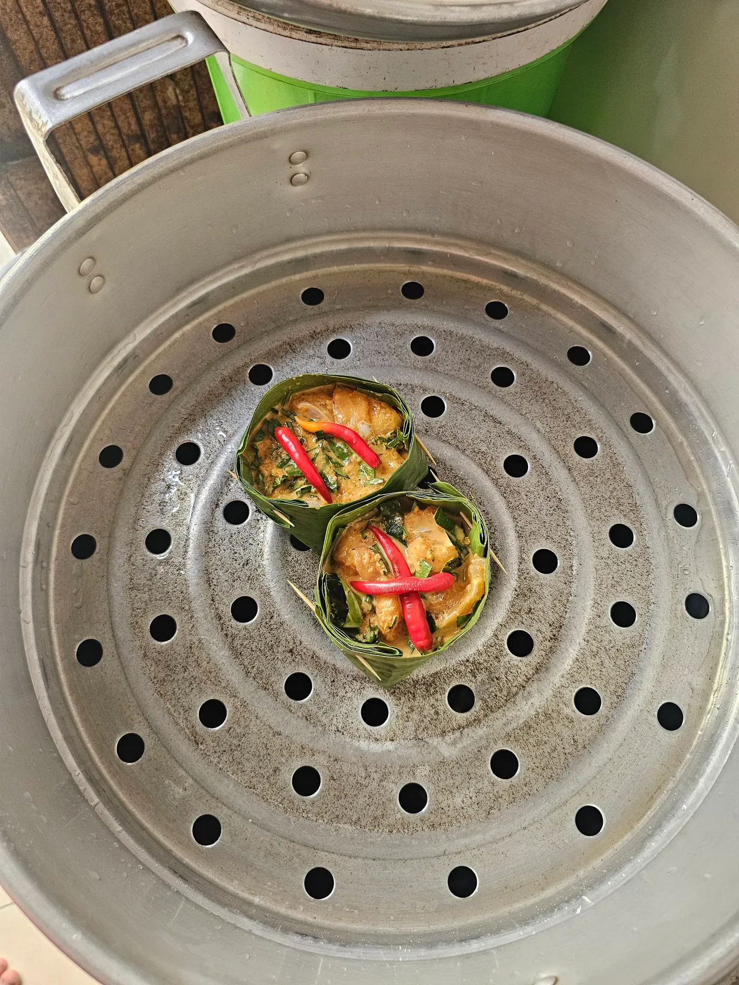 Deux amoks dans leurs coupelles en feuille de bananier, décorés de piment rouge, posés dans un panier vapeur en aluminium