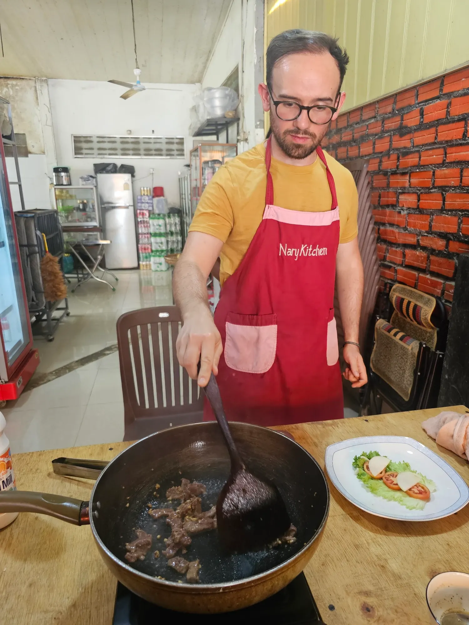 Antoine remue des lamelles de bœuf dans une poêle avec une spatule, au poste de cuisson