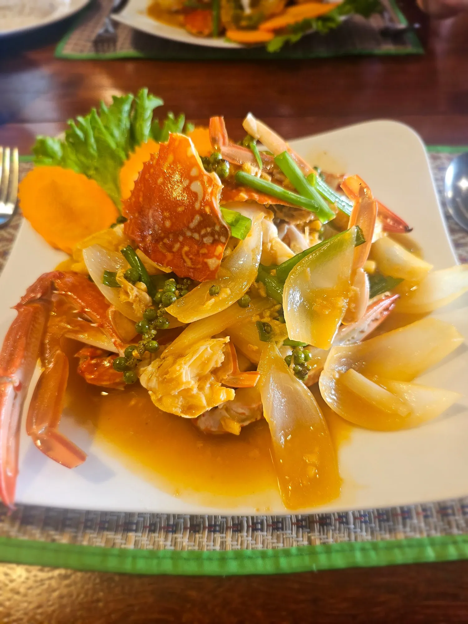 Le crabe au poivre vert de Kampot servi au Magic Crab, à Kep, sur une assiette carrée avec des oignons, de la ciboule et des grappes de poivre vert