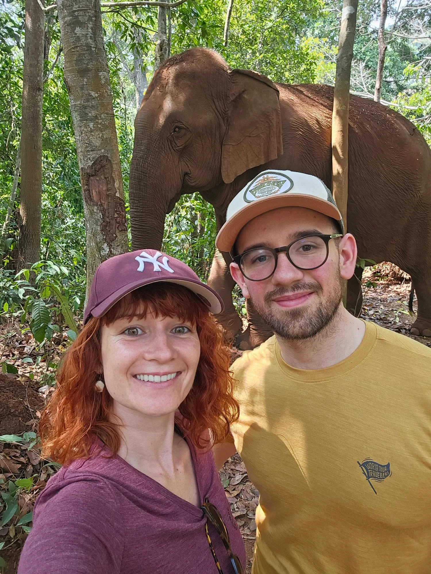 Selfie de Ségolène et Antoine, souriants, devant un éléphant d'Asie au milieu des arbres de la jungle du Mondulkiri
