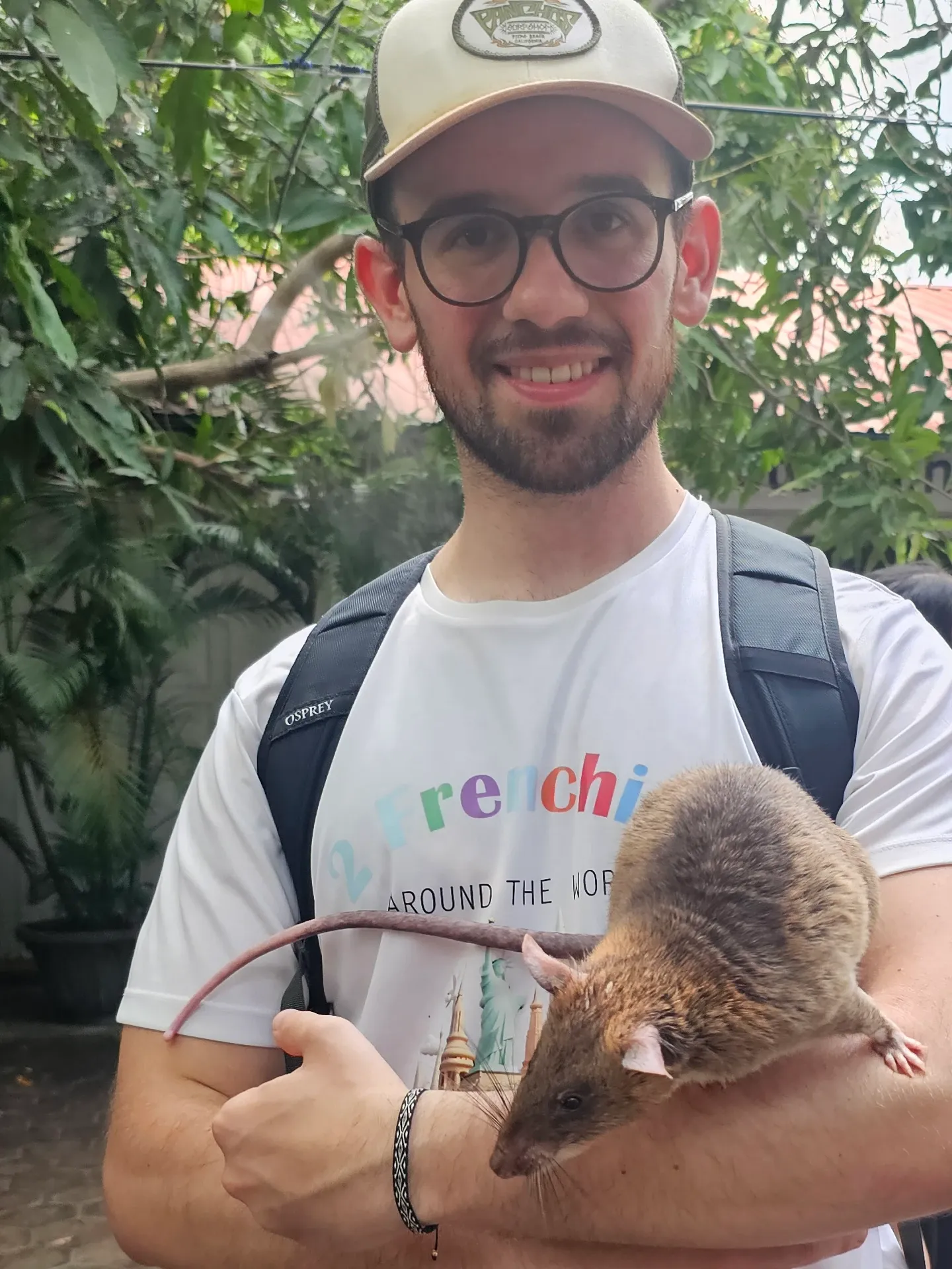 Antoine, souriant, porte un rat géant sur son avant-bras dans le jardin de l'Apopo Center