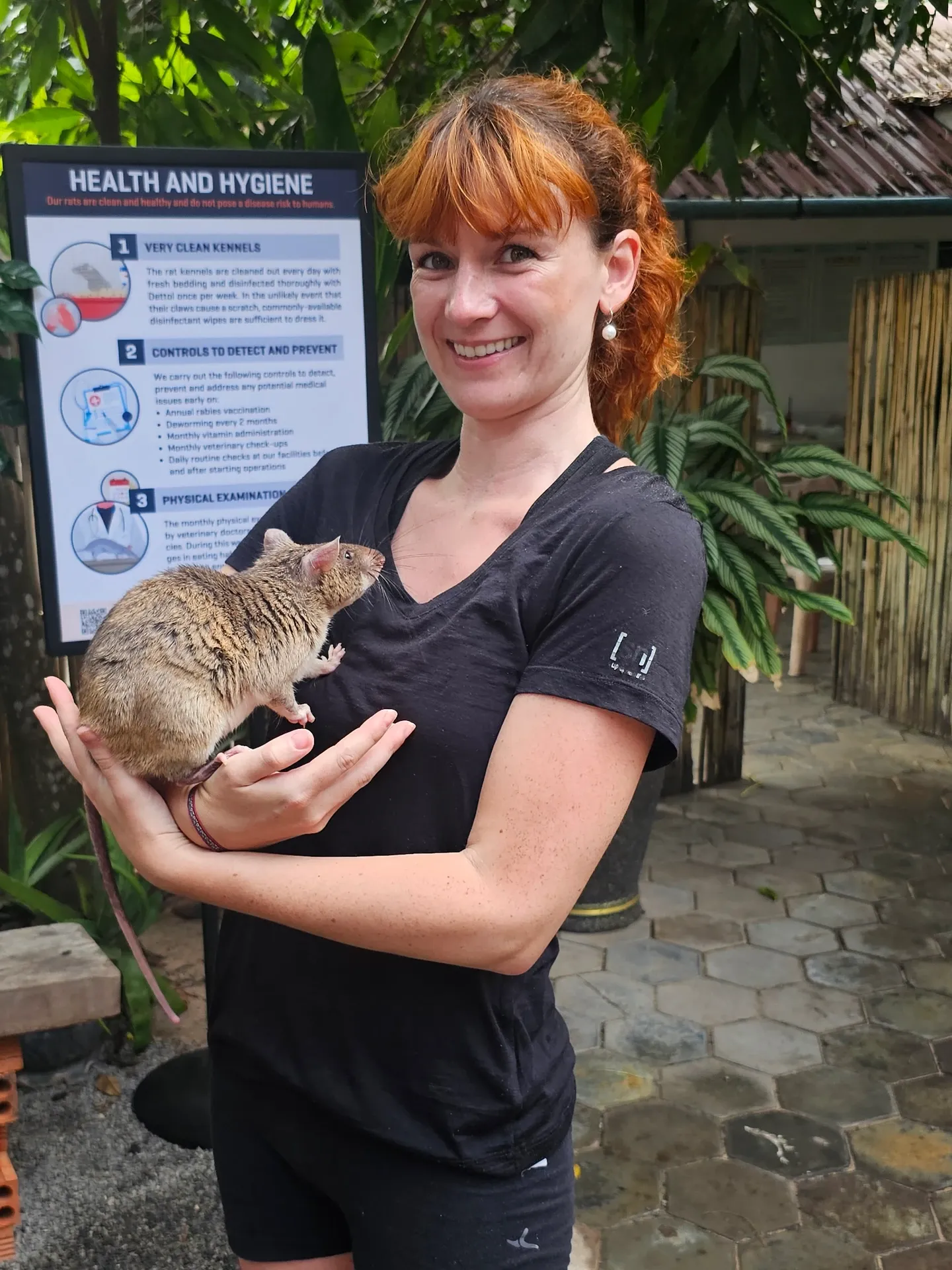 Ségolène, souriante, tient un rat géant contre elle dans le jardin de l'Apopo Center