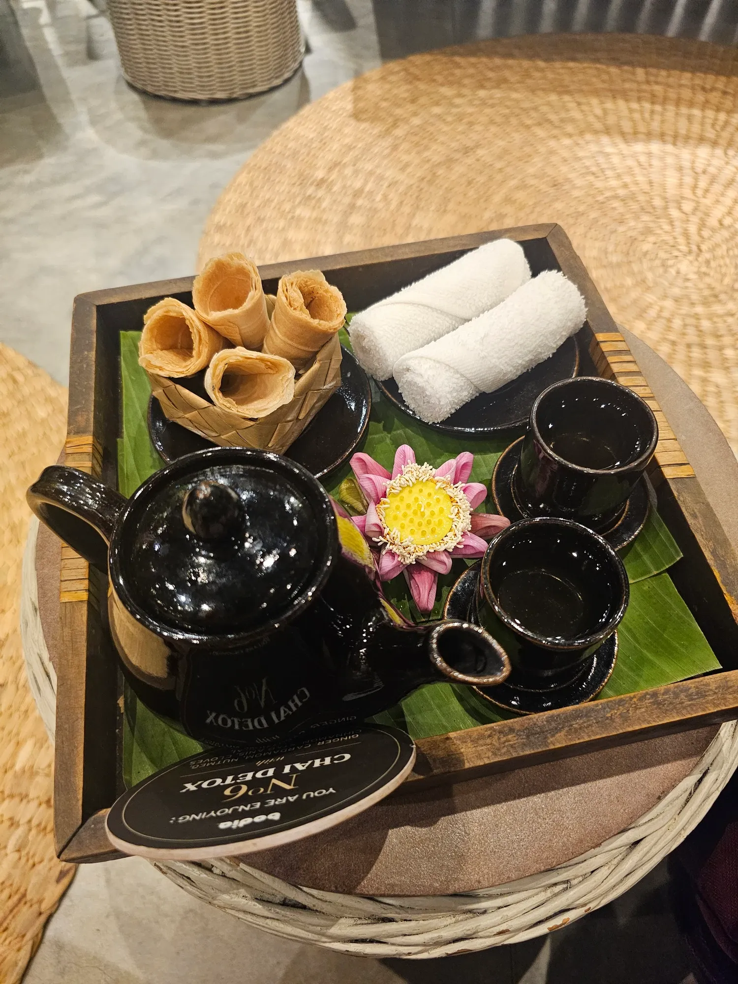 Plateau en bois chez Bodia Spa avec une théière noire, deux tasses, des biscuits roulés, deux serviettes roulées et une fleur de lotus