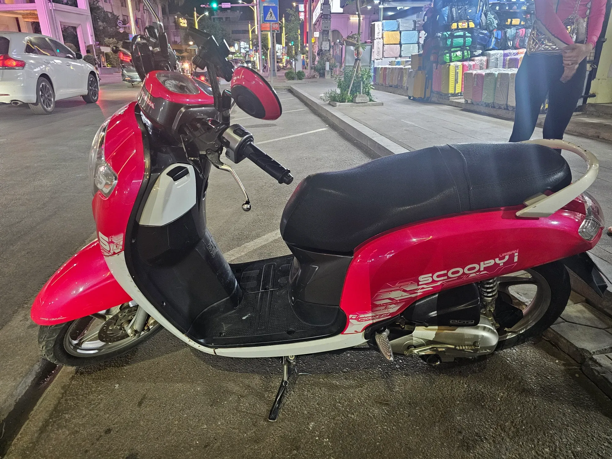 Scooter rose et blanc garé le long d'un trottoir de Siem Reap, le soir, devant une boutique de valises