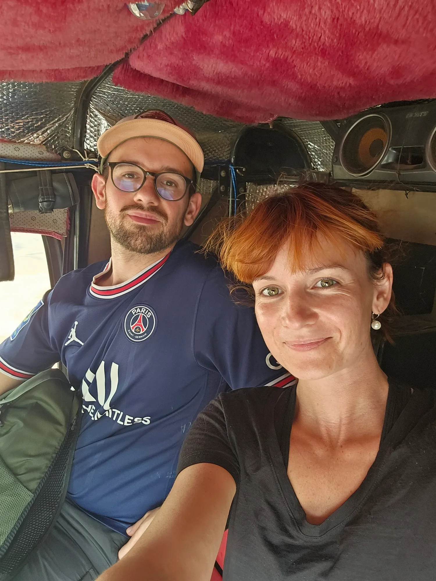 Antoine, en casquette et maillot du PSG, et Ségolène, souriants, assis à l'arrière d'un tuktuk au plafond garni de moumoute rose